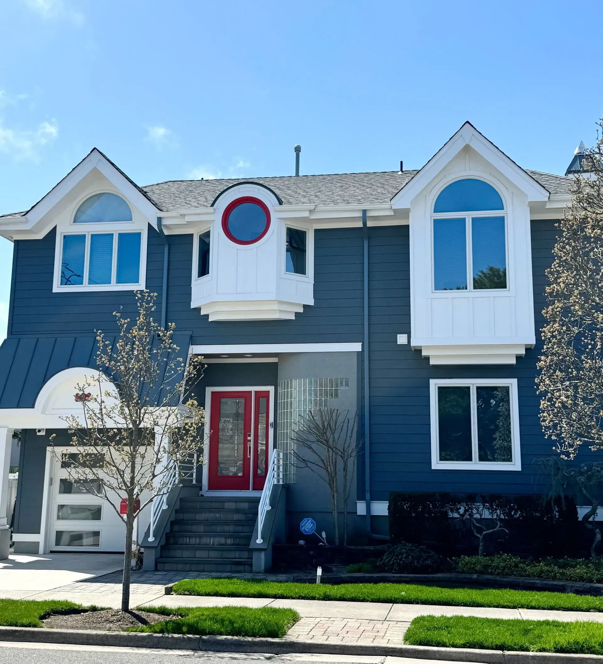 Two-story blue house with white trim. Red front door, arched windows, and small front yard with green grass.
