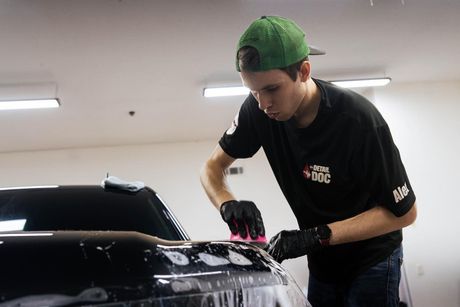 A man in a green hat is cleaning the hood of a car.