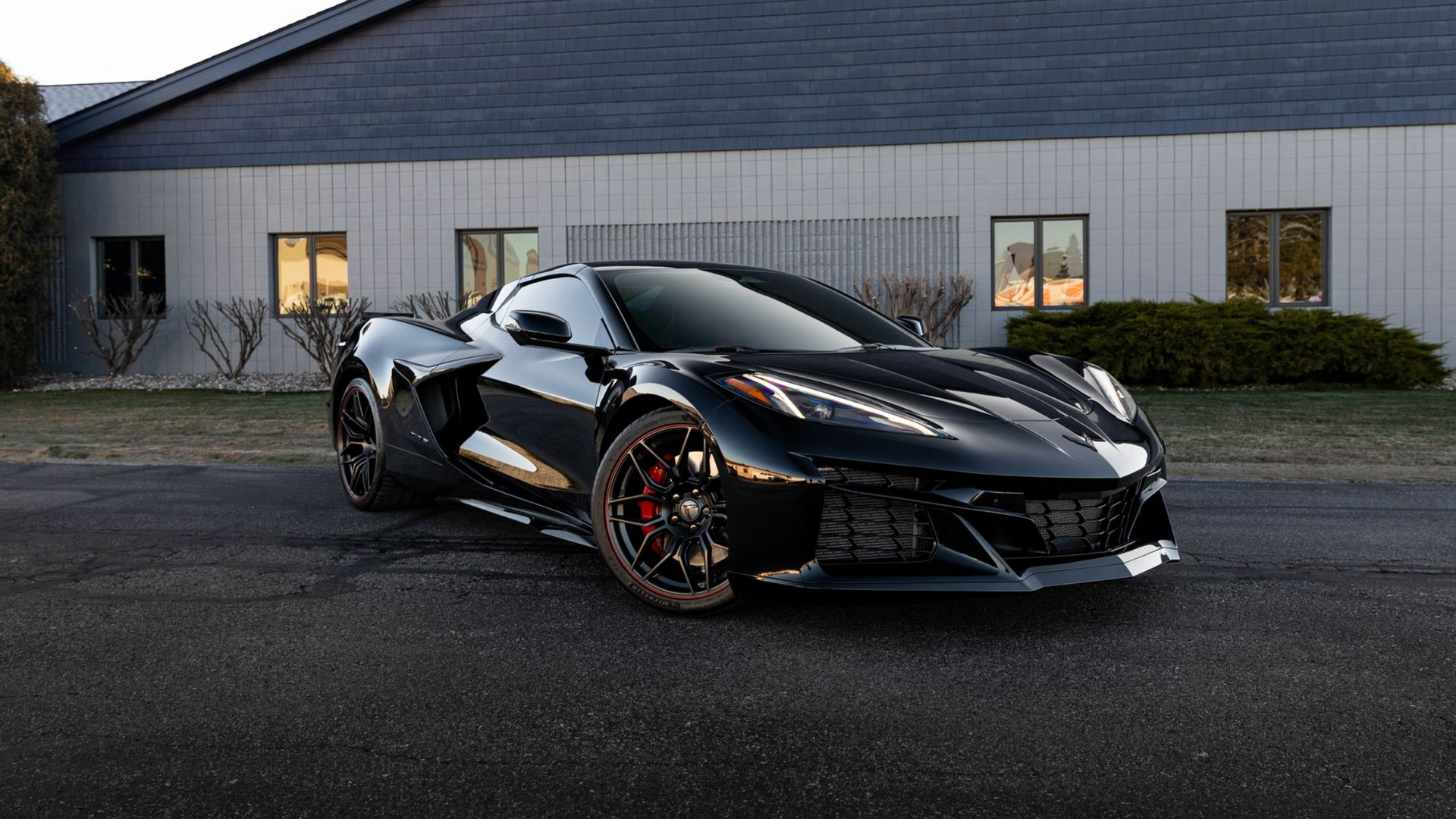 Black Corvette sports car parked in front of a building with windows, evening light.