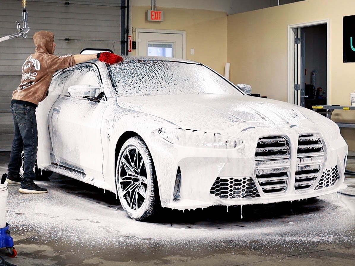 A man is washing a car with foam in a garage.