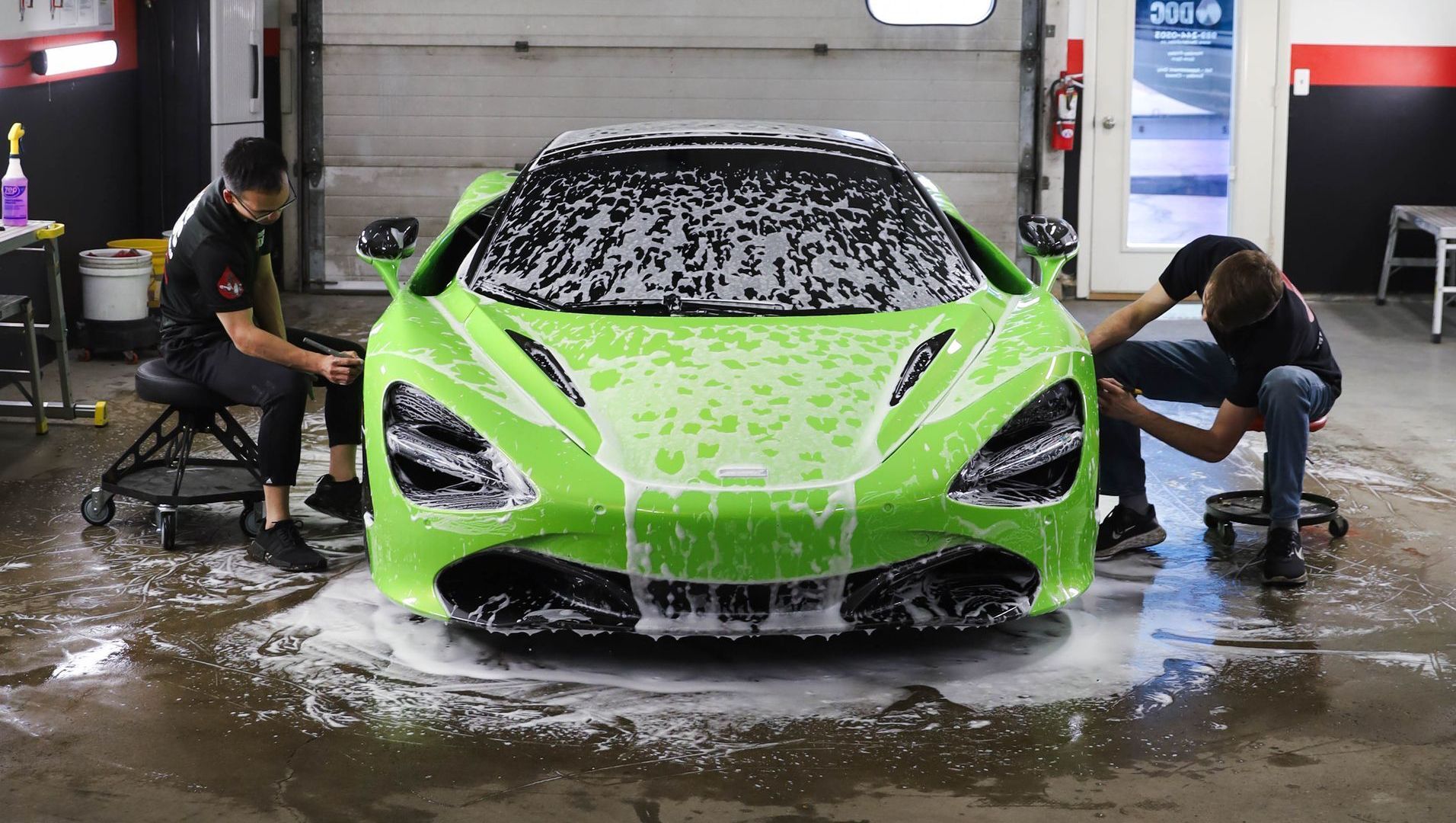 Two men are washing a green sports car in a garage.