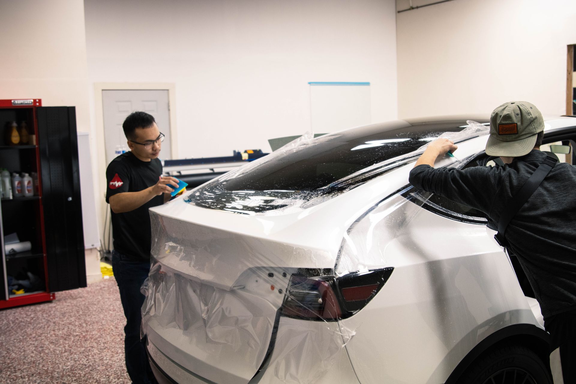two men are wrapping a white tesla model 3 in a garage .