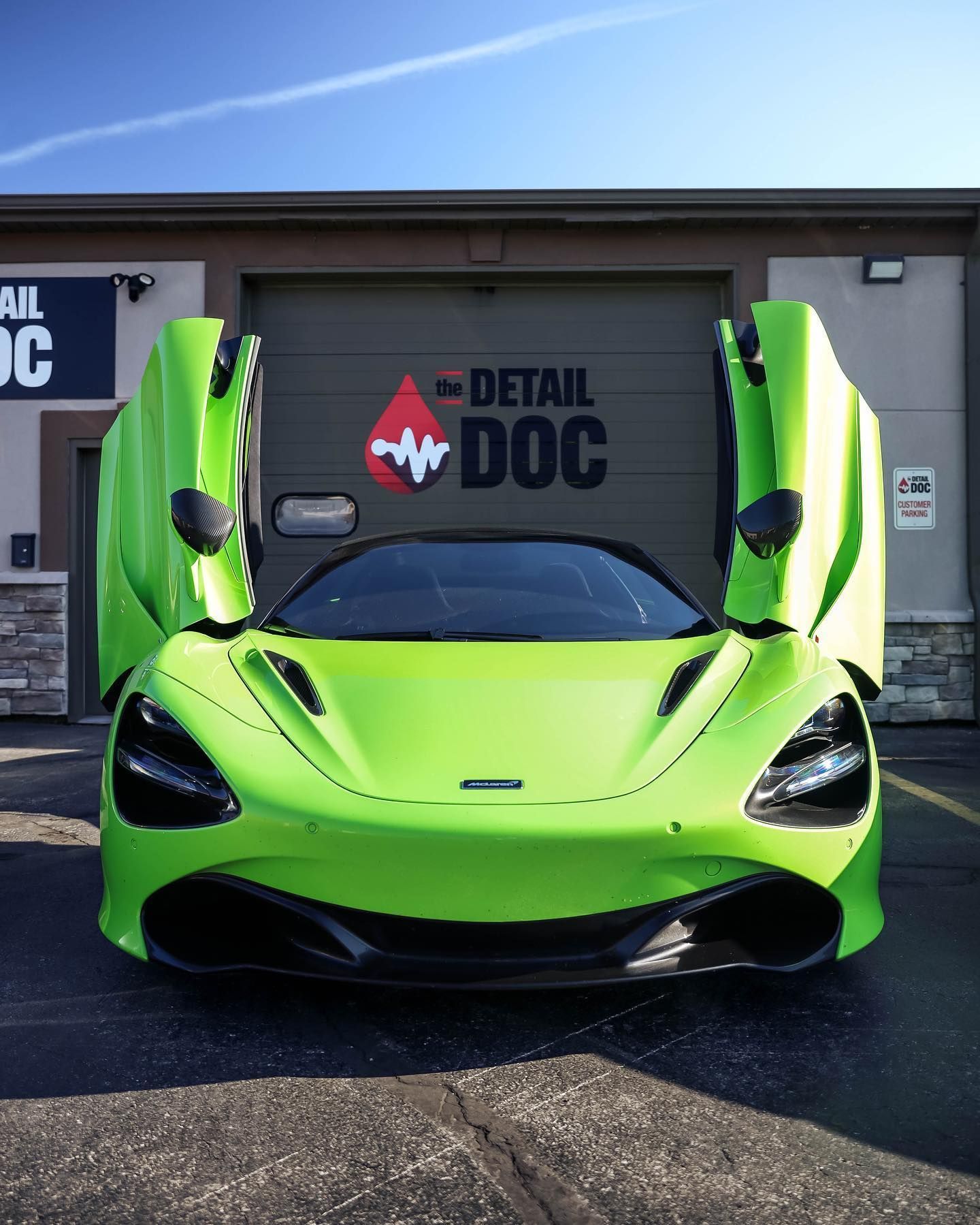 A green sports car is parked in front of a building that says detail doc