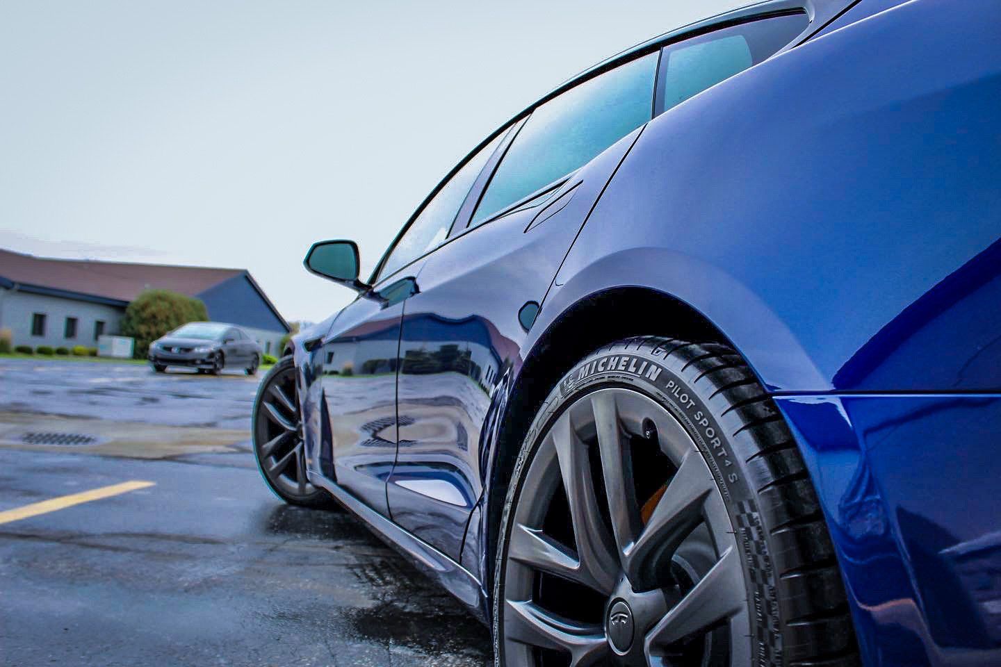 a blue car with black wheels is parked in a parking lot .