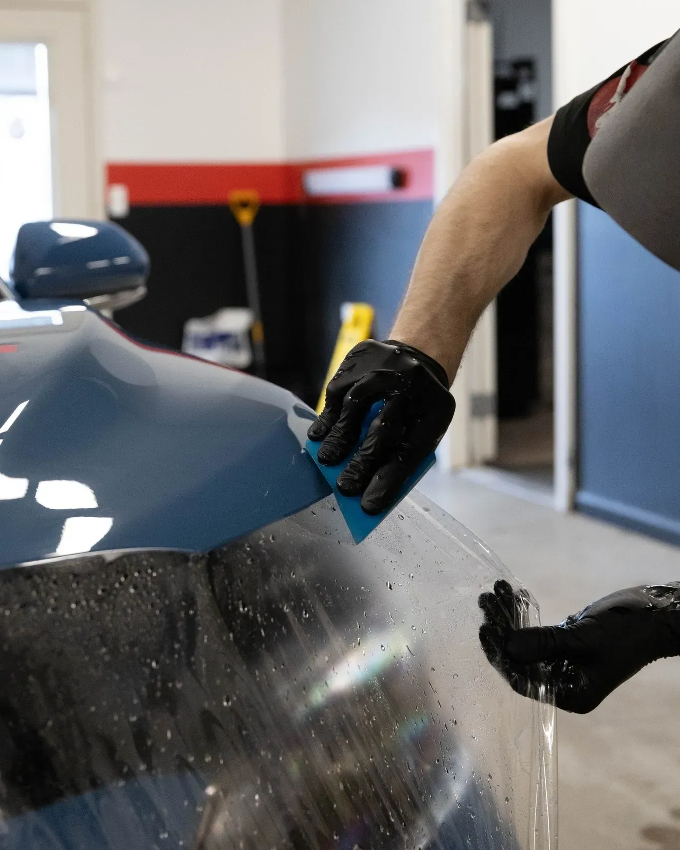 A person is applying protective film to the hood of a car.