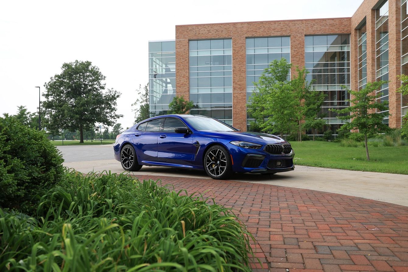 a blue bmw m8 is parked in front of a large building .
