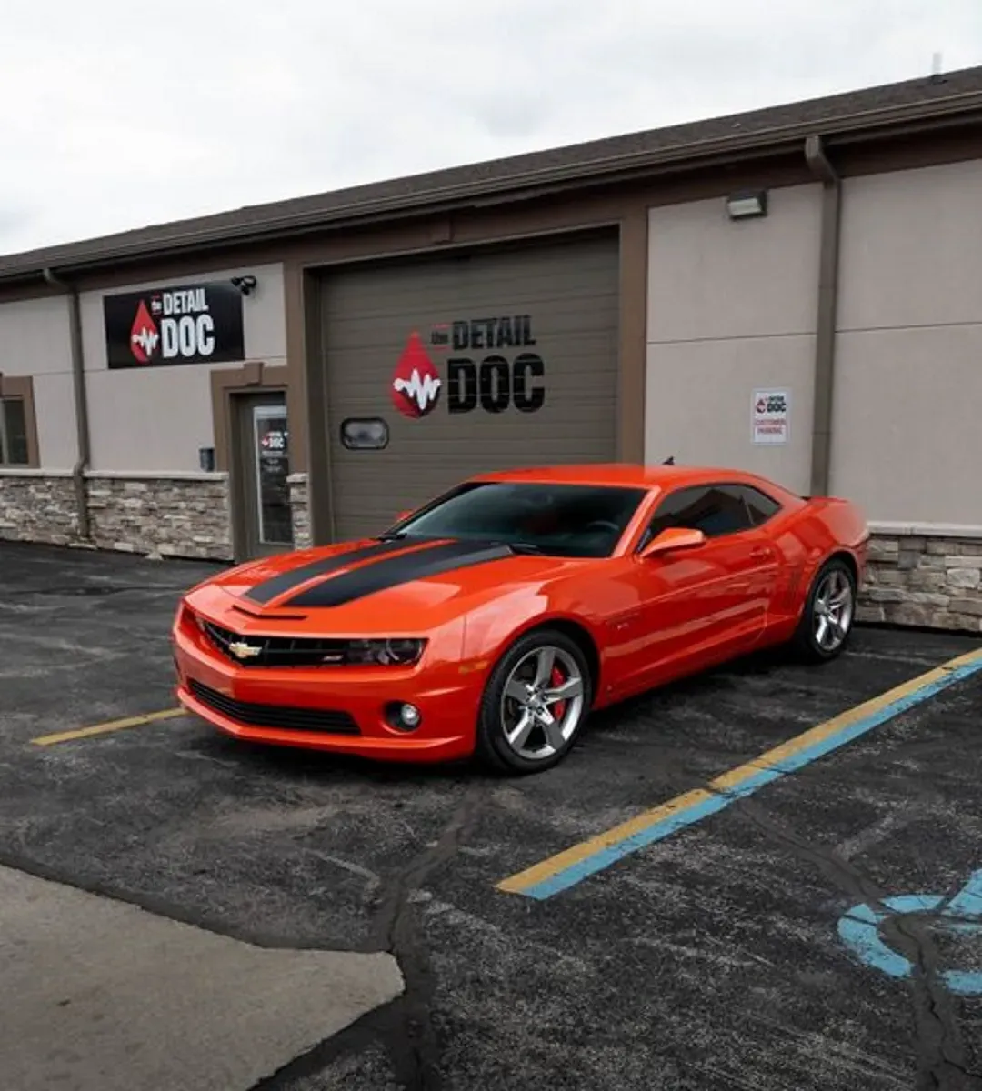 An orange car is parked in front of a building that says detail doc