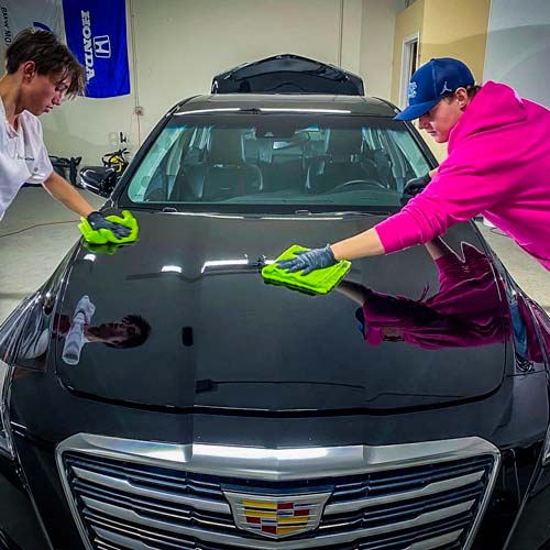 a man in a pink hoodie is cleaning the hood of a black car .