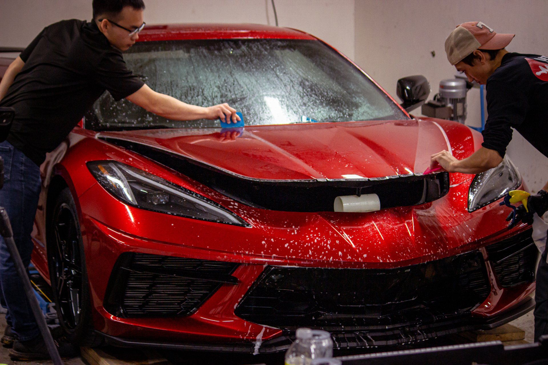 Two men are working on a red sports car in a garage.