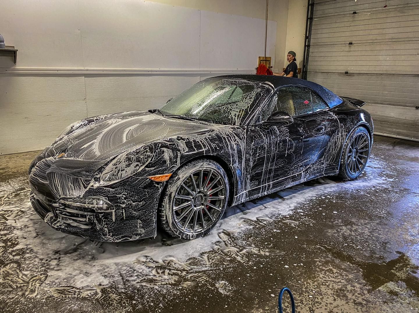 A black sports car is covered in foam in a garage.