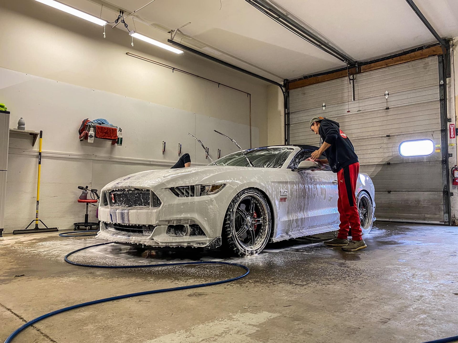 A man is washing a white mustang in a garage.