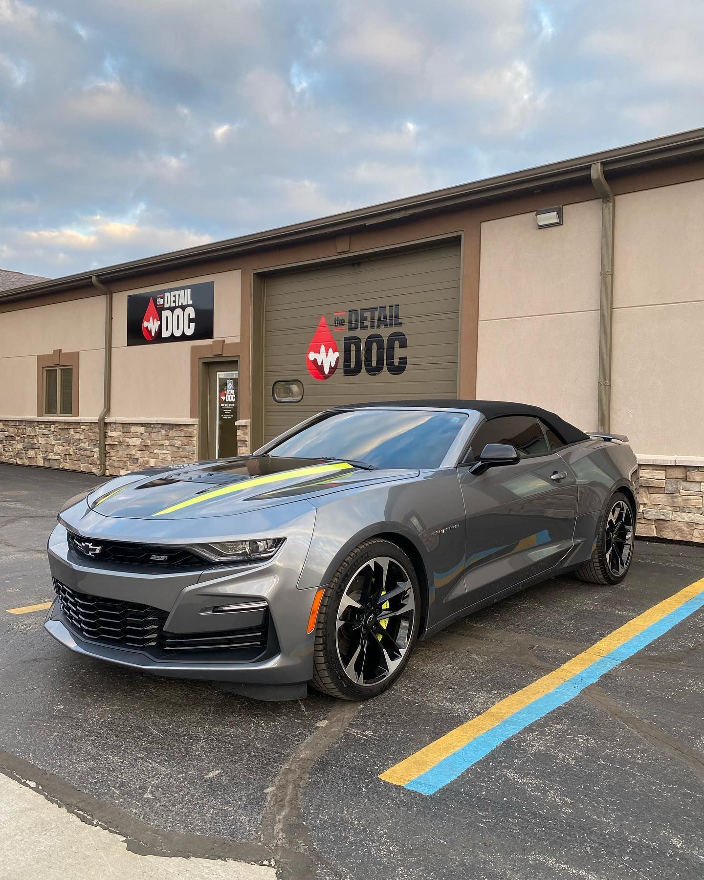 A gray car is parked in a parking lot in front of a building.