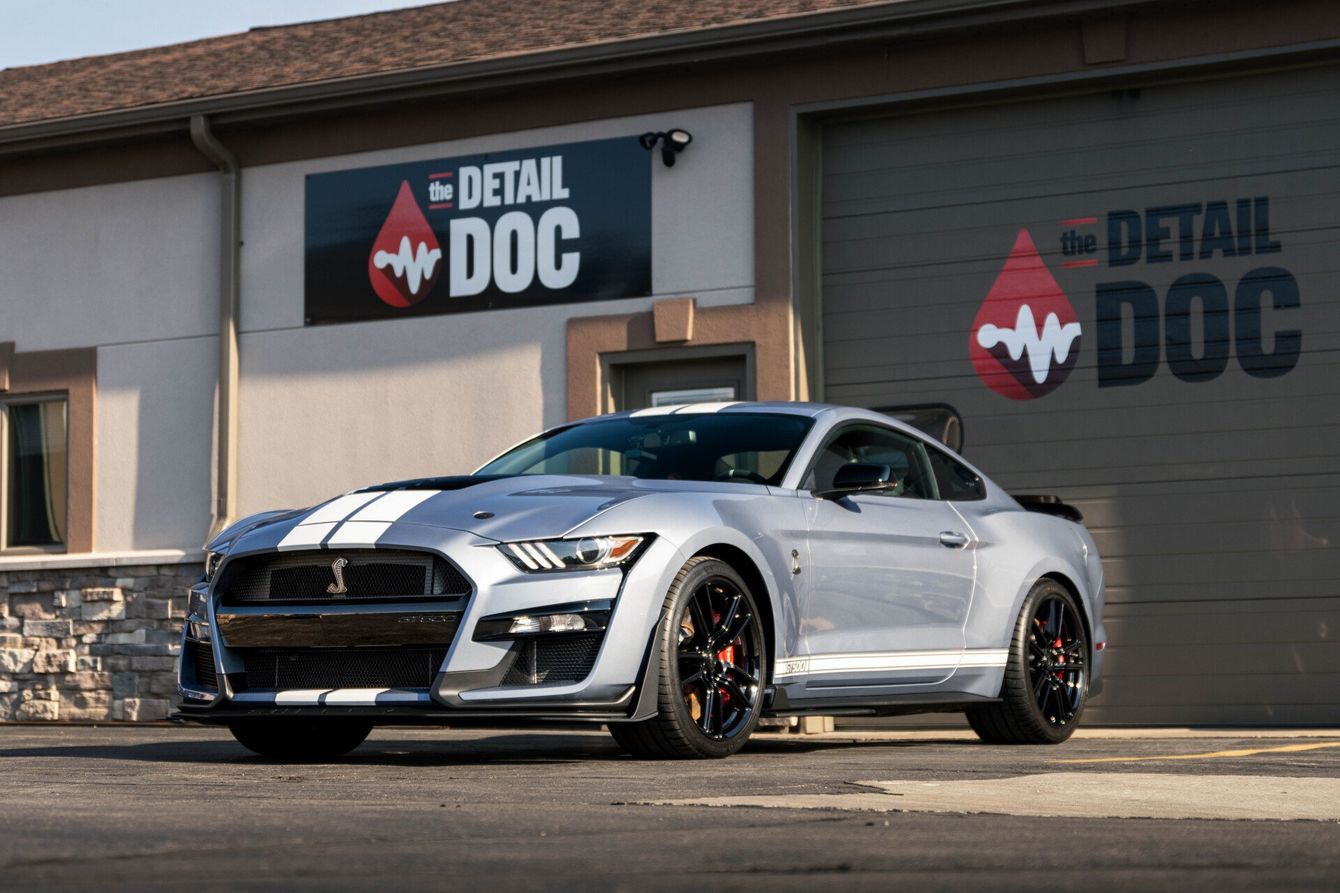 a silver mustang is parked in front of a building with a sign that says detail doc .