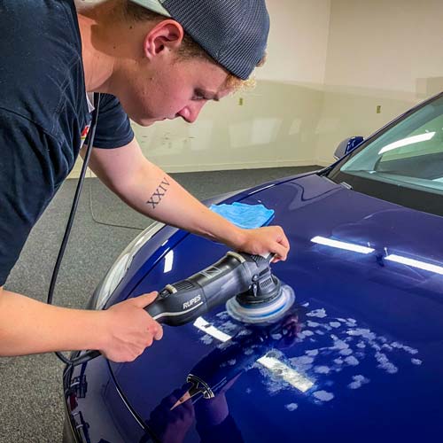 a man is polishing a blue car with a machine .