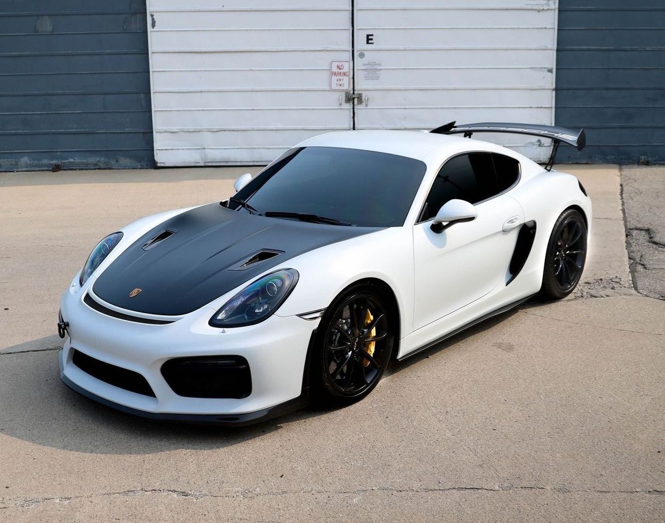 a white sports car with a black hood is parked in front of a garage .