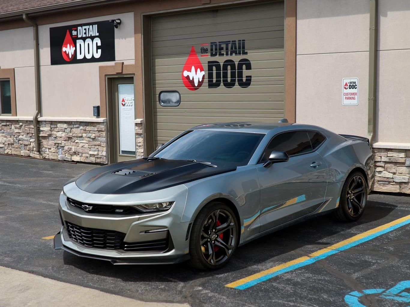 A silver car is parked in front of a building that says detail doc.