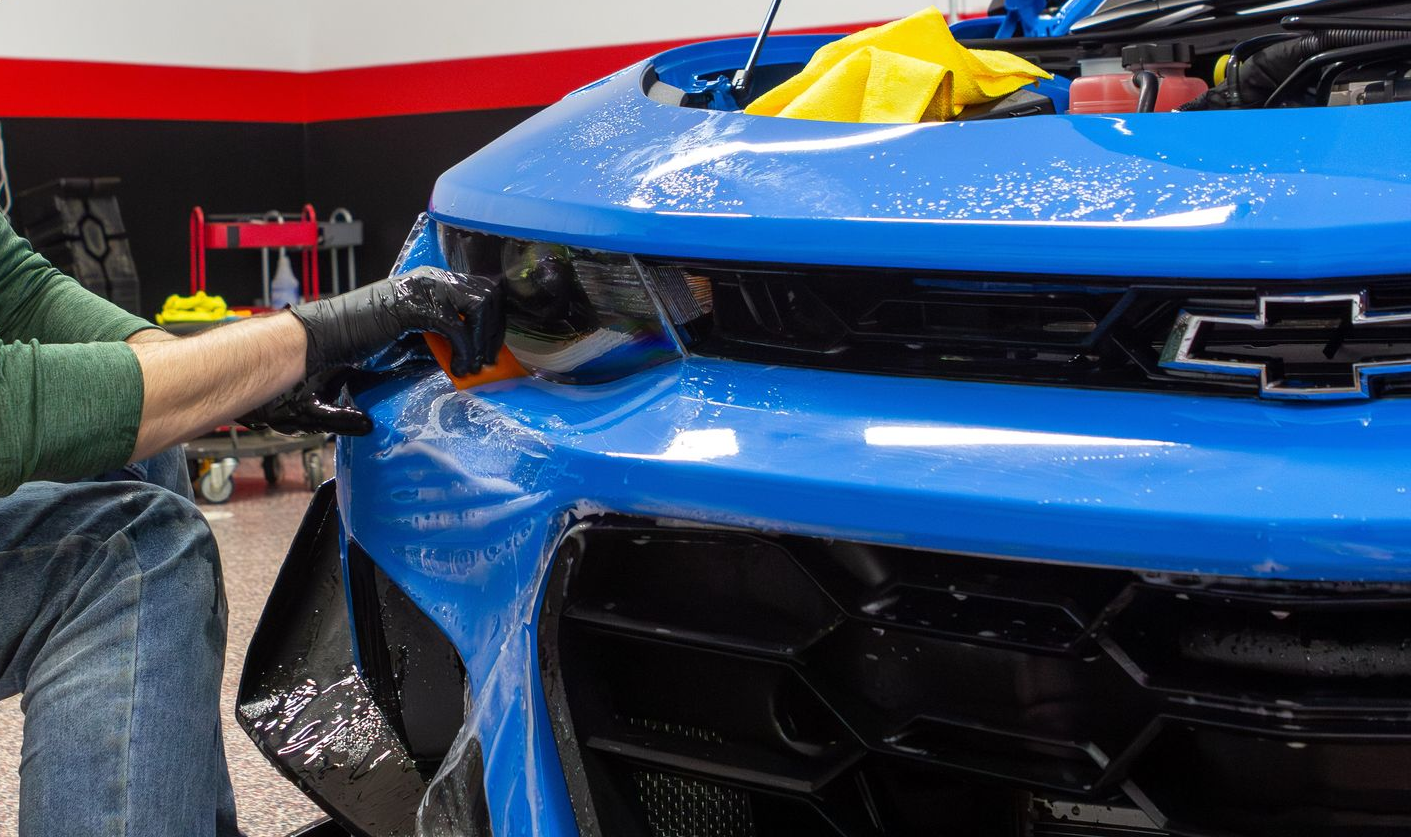 Person applying blue wrap to the front of a blue Chevrolet Camaro.