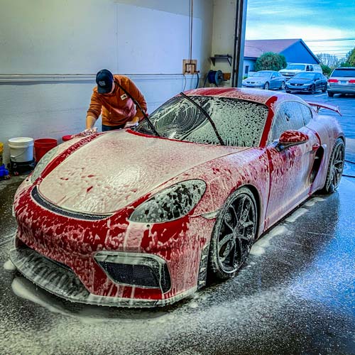 a man is washing a red sports car with foam in a garage .