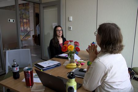 Two women sitting at a desk in front of a nachw banner