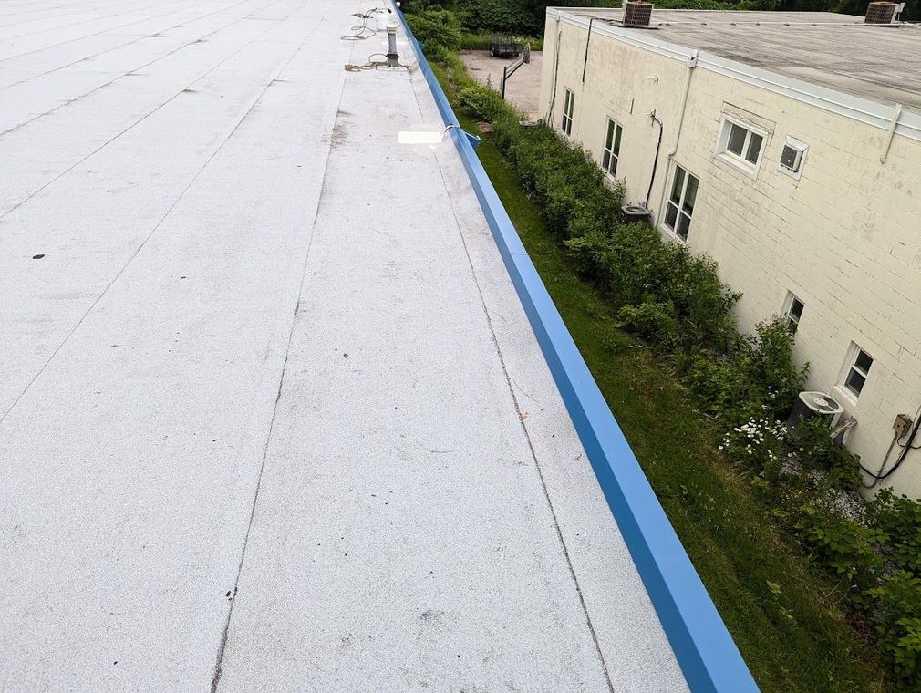 White flat roof next to blue edge and greenery along a beige building.