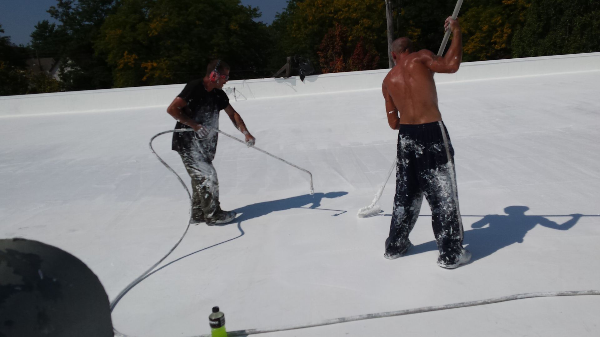 Two men coat a white roof with white material on a sunny day.