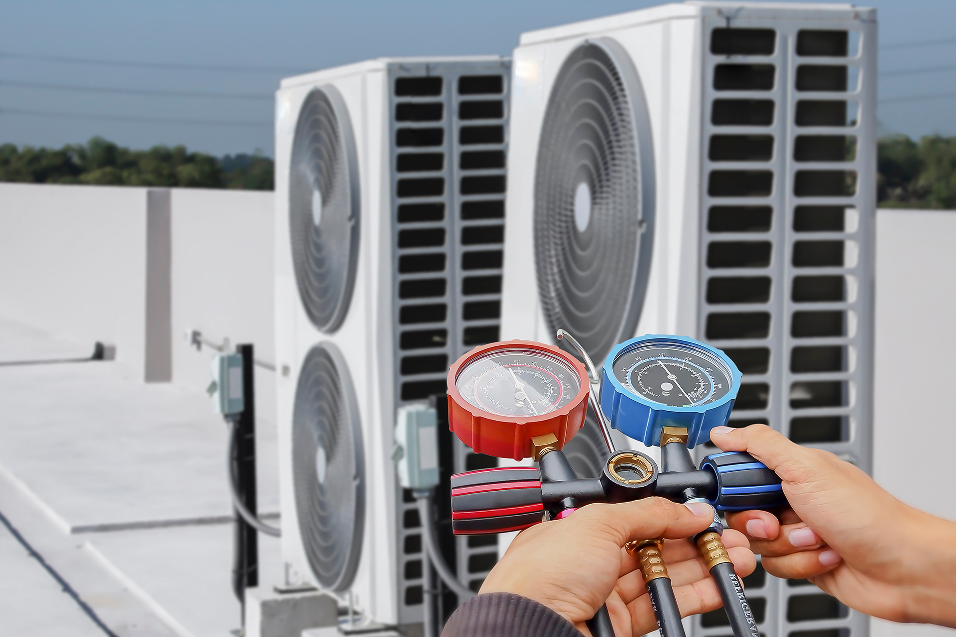 A person is holding a vacuum gauge in front of two air conditioners.