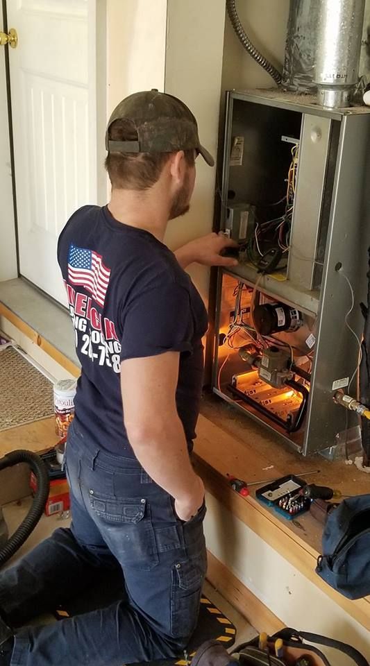 A man is kneeling down in front of a fireplace while working on it.