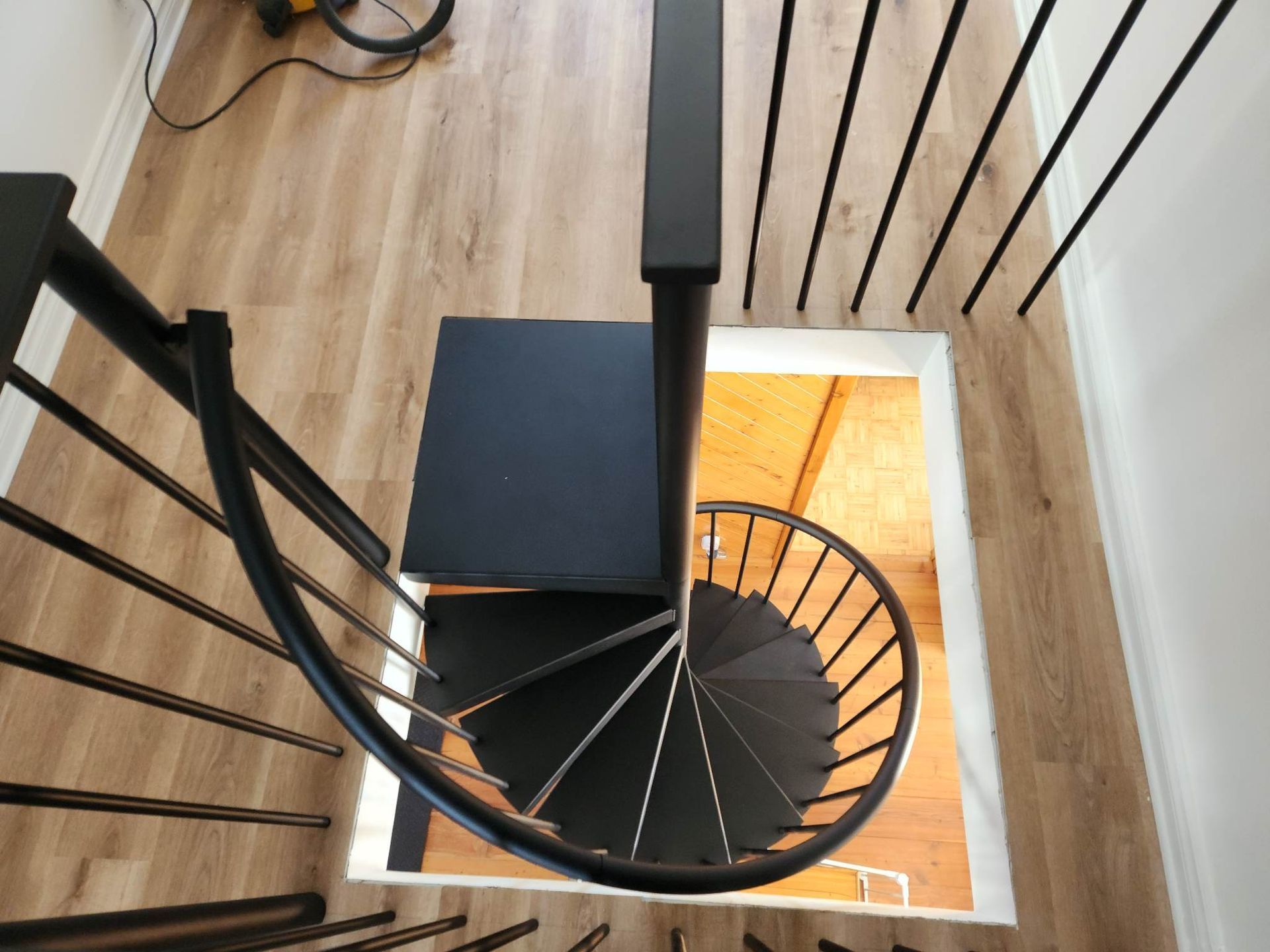 Escalier en colimaçon noir avec rampe noire et plancher en bois vu du dessus.