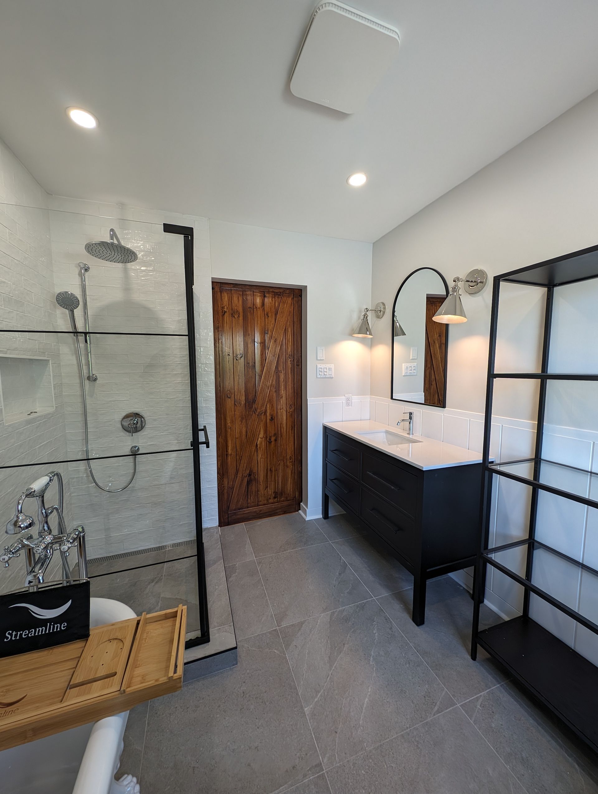 Salle de bain moderne avec douche, vanité, porte rustique et étagères noires.