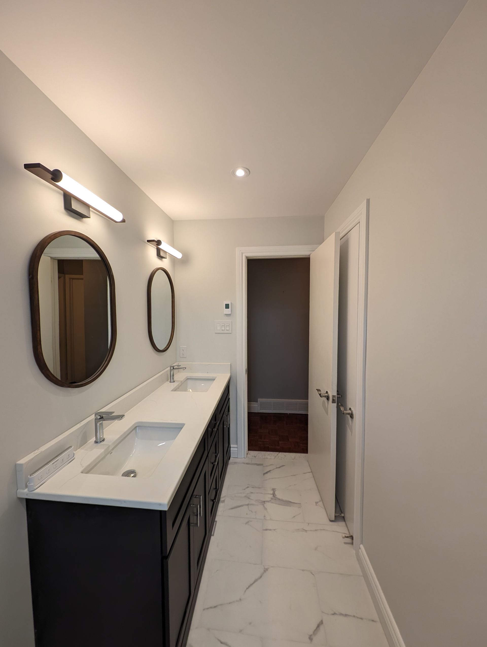 Salle de bain avec vanité sombre, miroirs ovales et sol en marbre blanc.