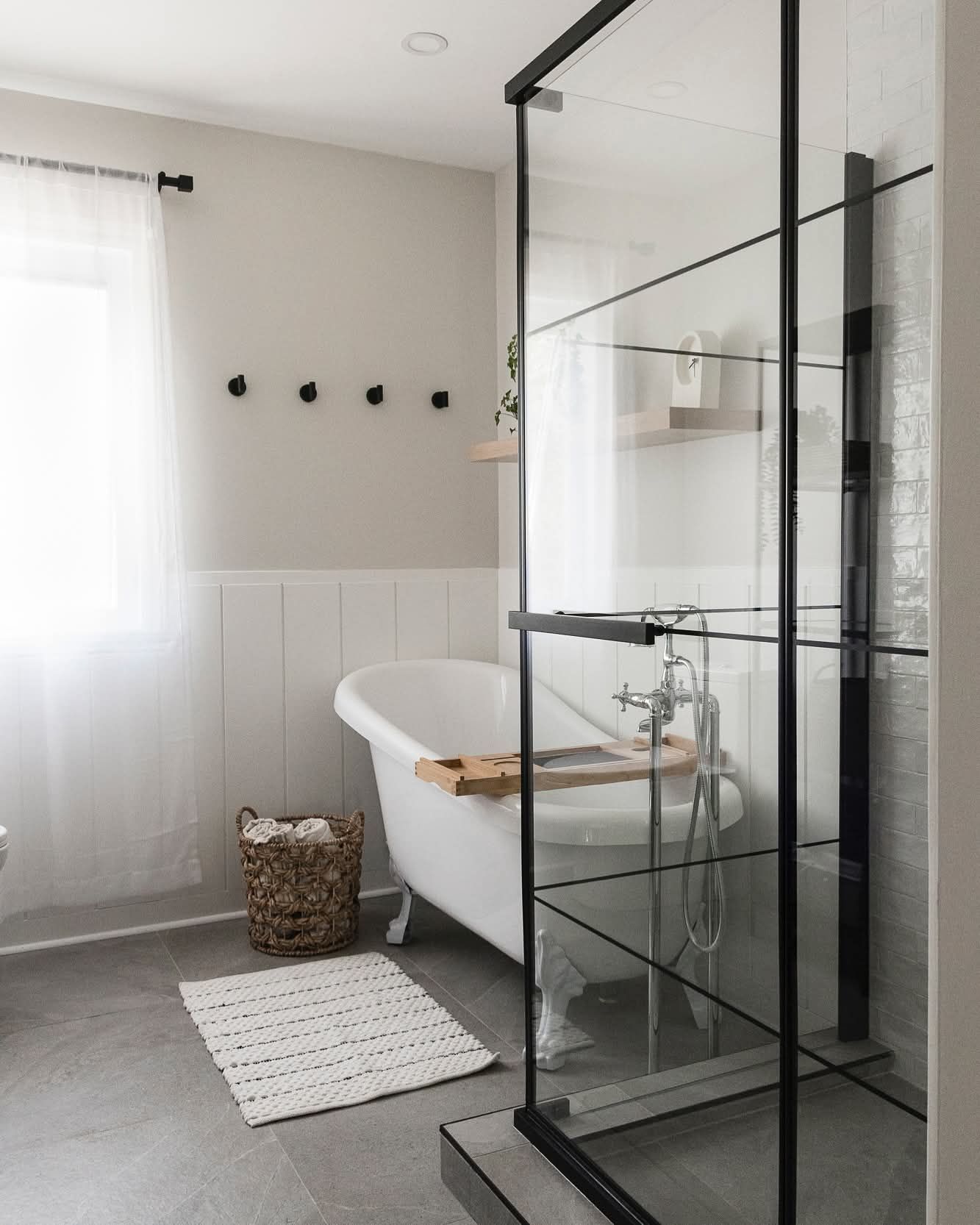 Salle de bain avec baignoire autoportante, douche en verre, murs blancs et gris et tapis tissé.
