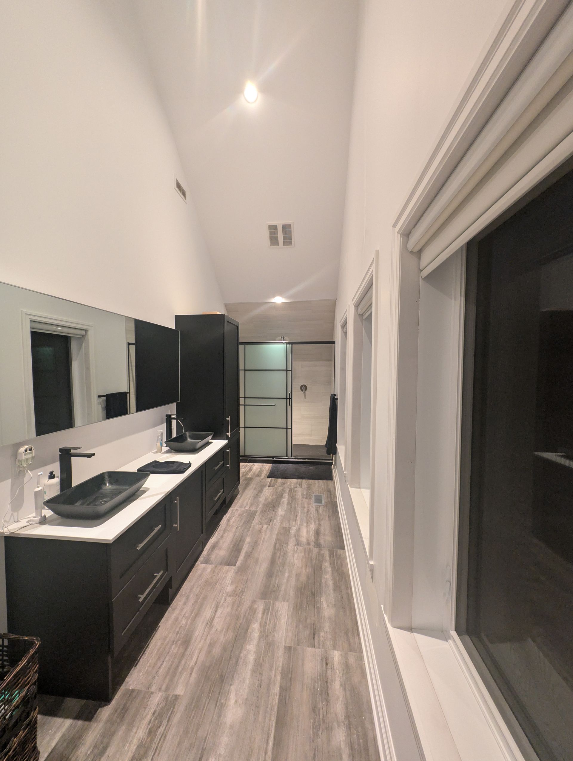 Salle de bain moderne avec vanité noire, lavabos, long miroir et fenêtre.