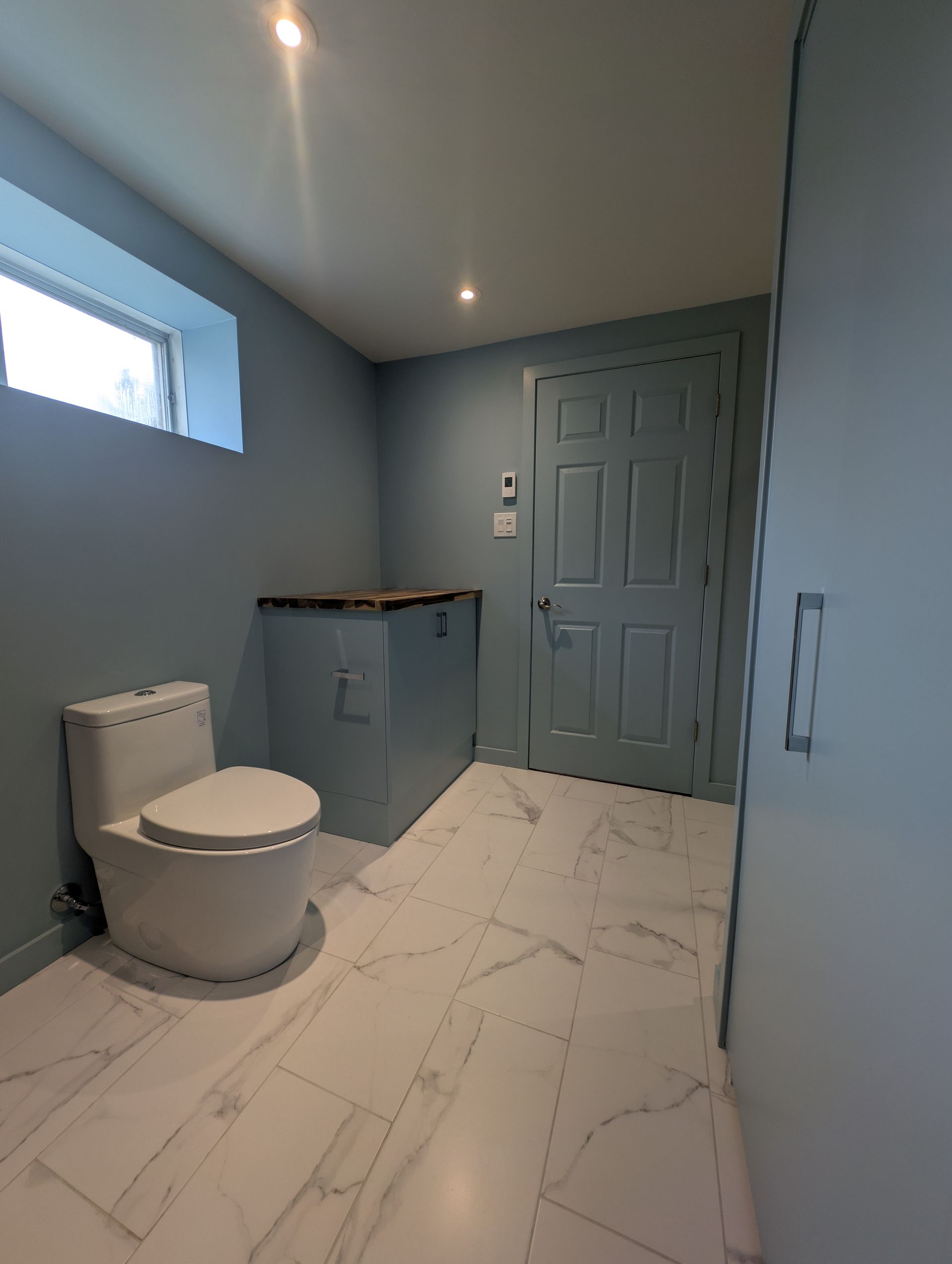 Salle de bain bleue avec sol en marbre, toilettes et porte.