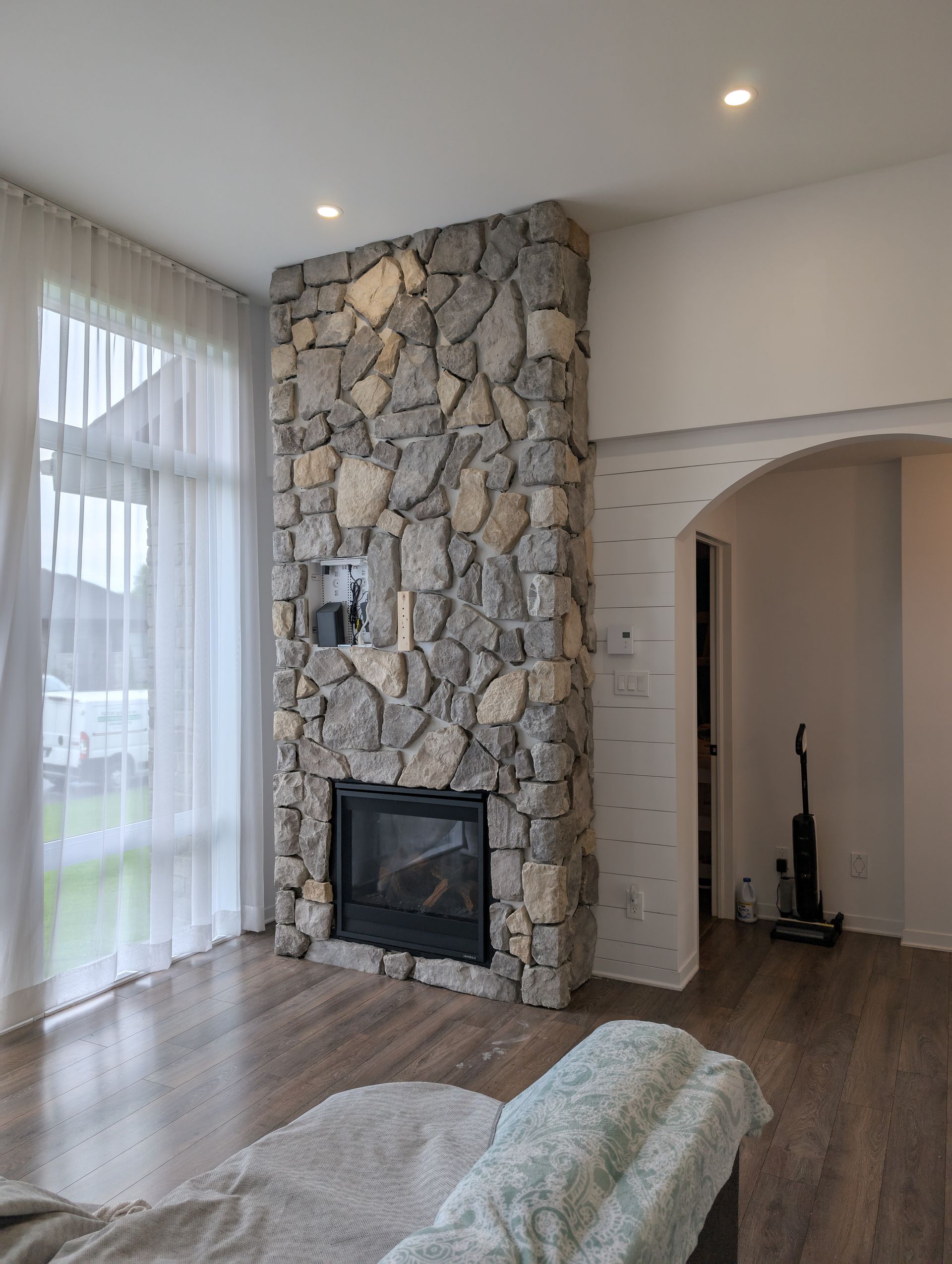 Cheminée en pierre dans un salon avec de grandes fenêtres, un aspirateur et une arcade.