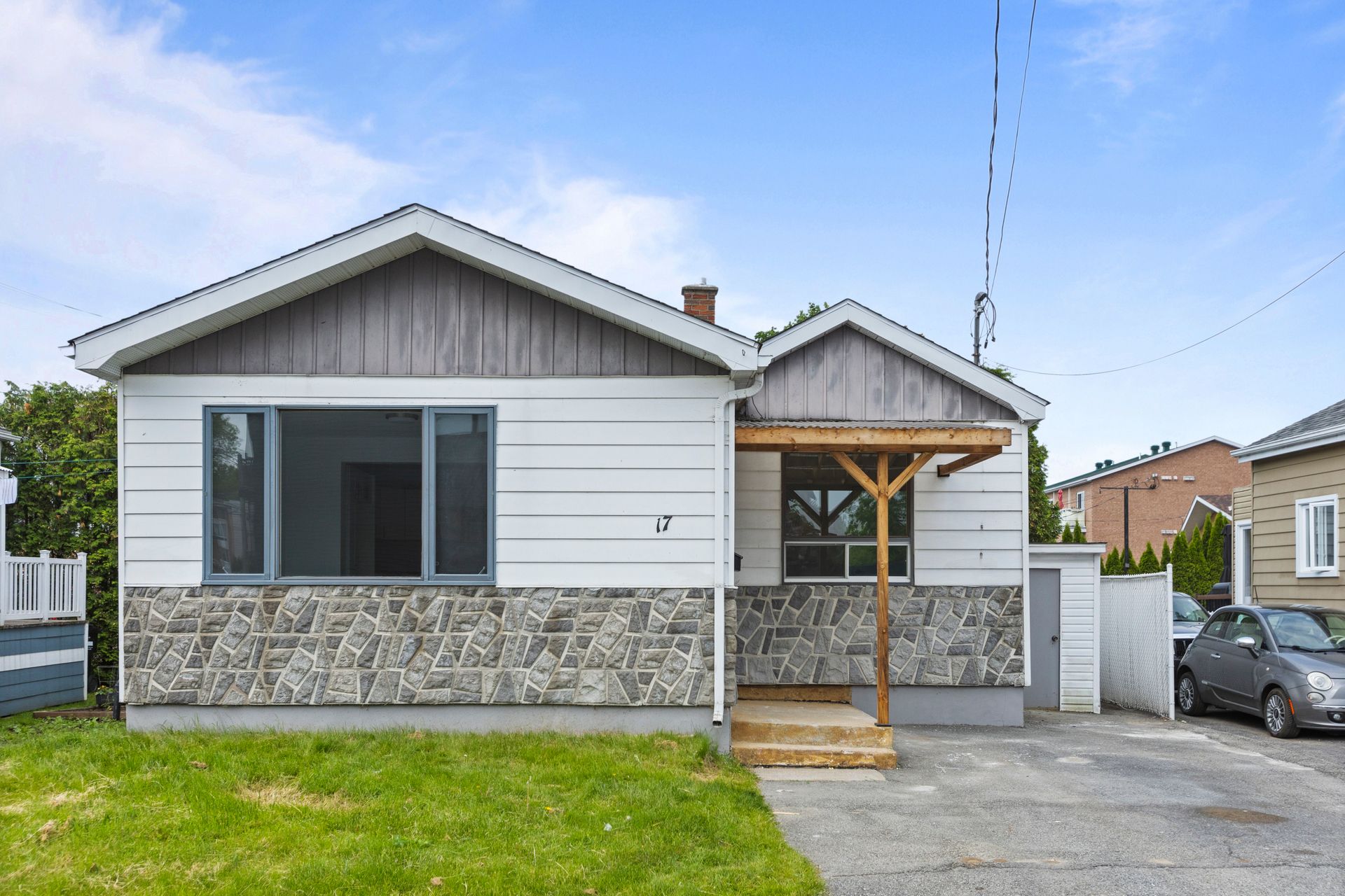 Petite maison blanche avec façade en pierre et porche en bois par une journée ensoleillée.