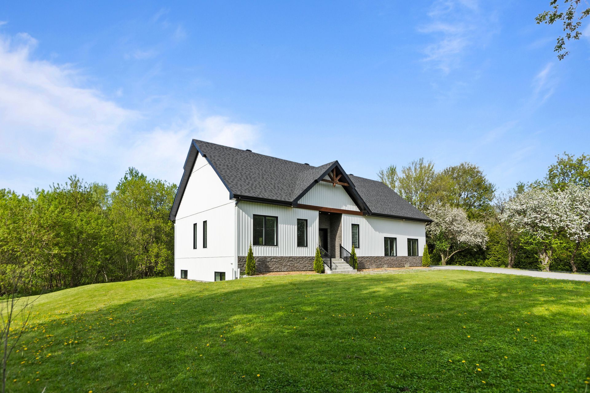 Maison blanche sur une colline herbeuse sous un ciel bleu, arbres en arrière-plan.