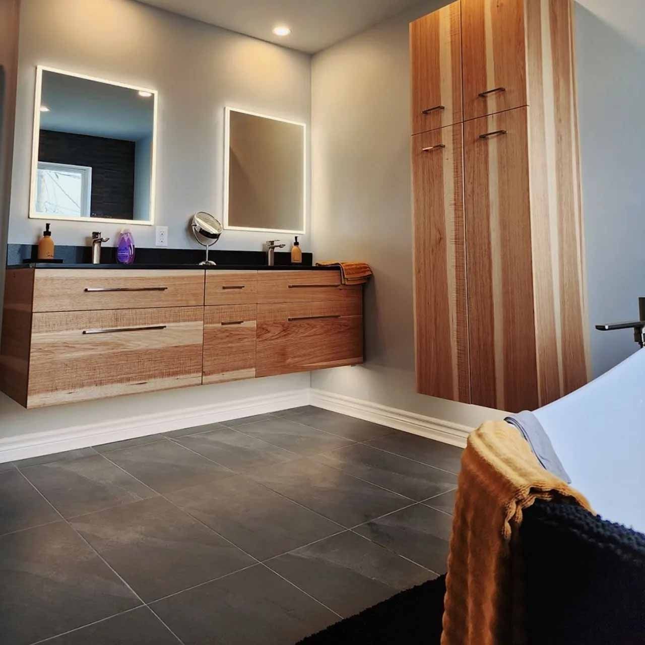 Salle de bain moderne avec vanité flottante en bois, miroirs et armoire de rangement; murs gris, sol foncé.