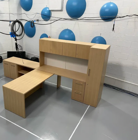 Light wood office desk with overhead storage and side cabinets; gray floor, white wall, blue spheres.