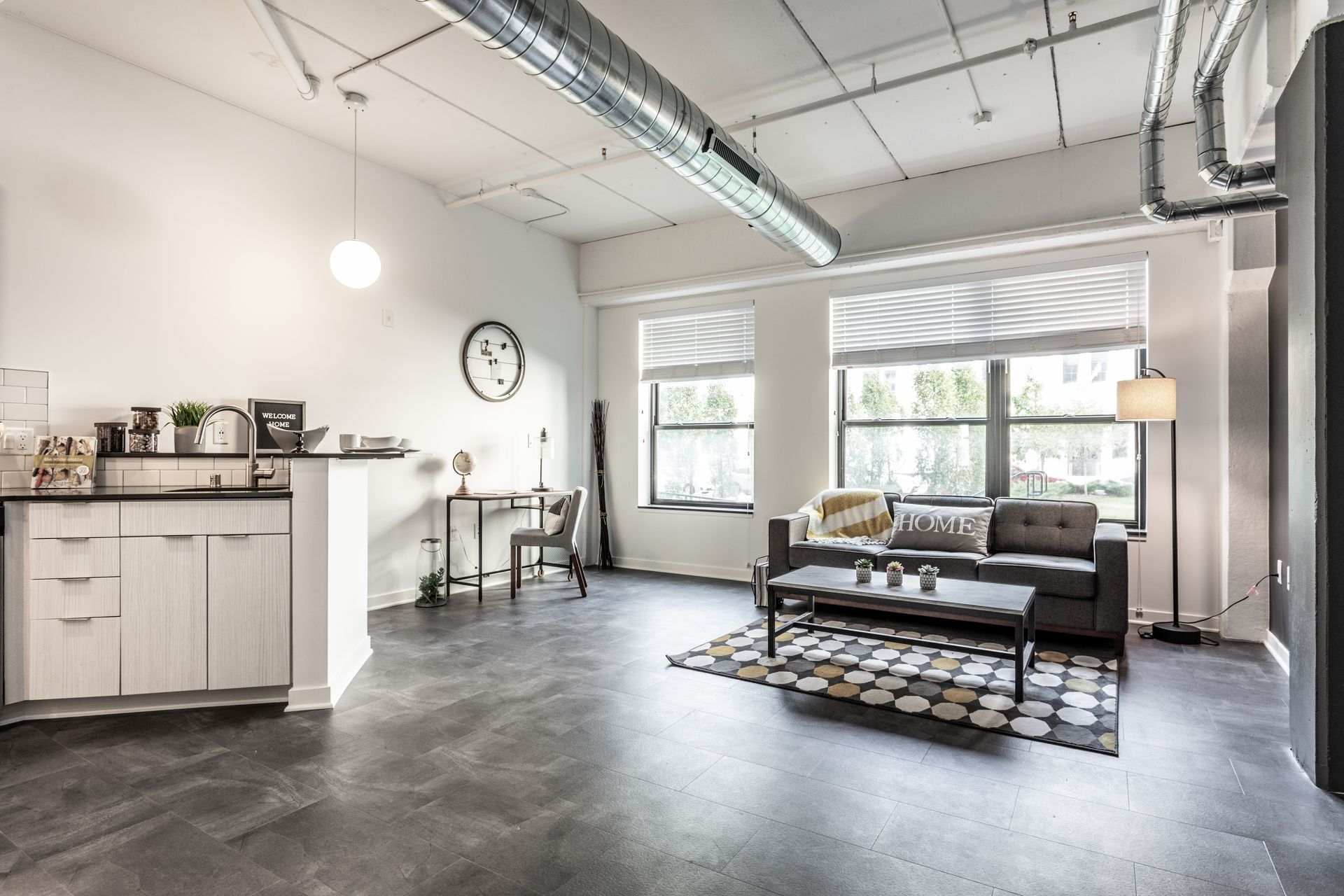 Loft apartment with concrete floor, white walls, and industrial style. Features living area, kitchen, and large windows.