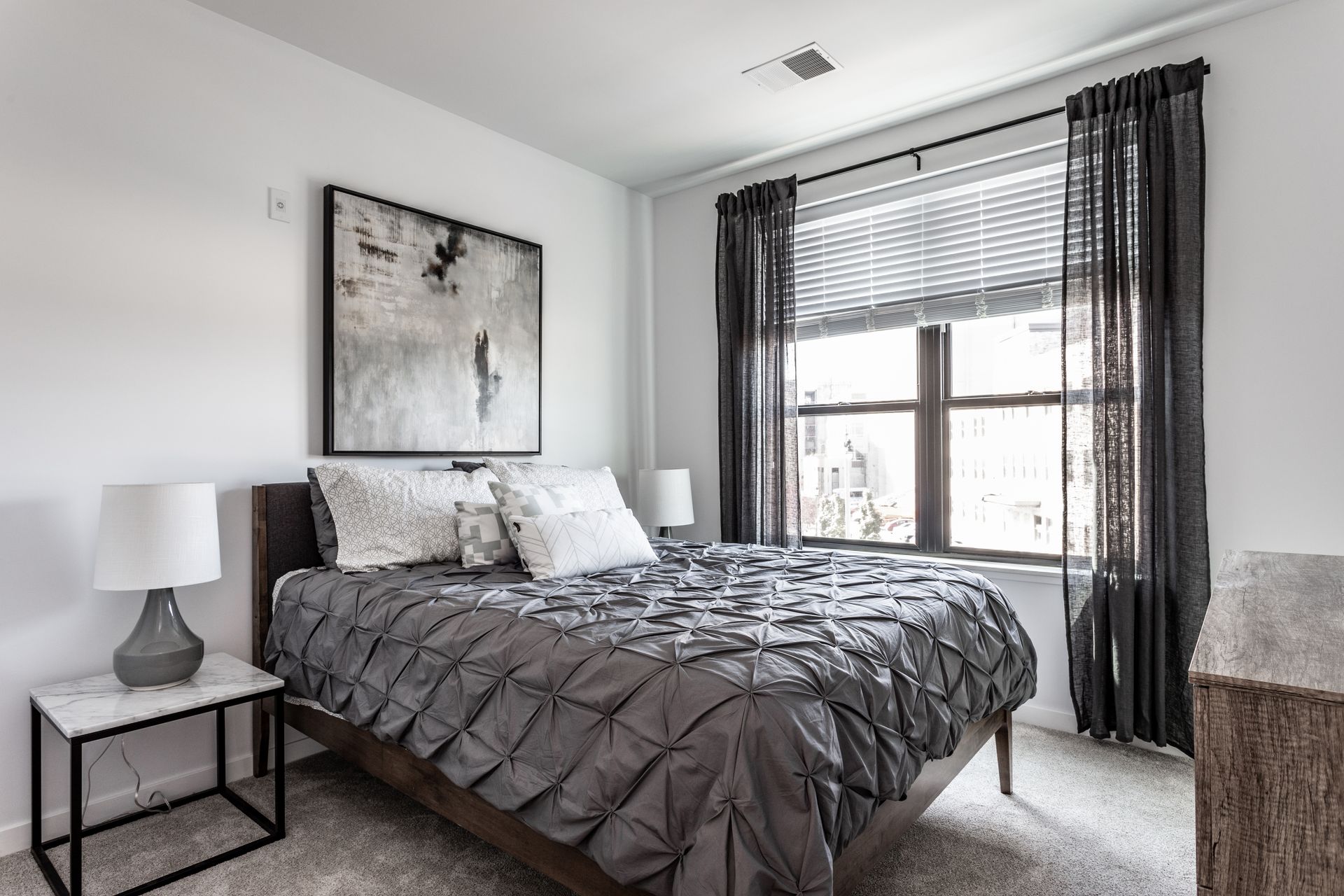 Bedroom with a gray bed, white walls, and a window with curtains.