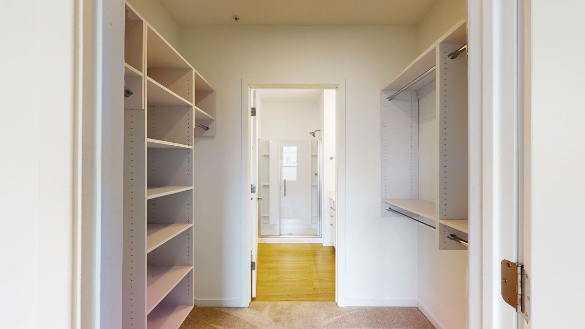 Here at Vim + Vigor Lofts in Wisconsin. A spacious walk-in closet features built-in shelving, hanging rods, soft carpeting, and easy access to the bathroom.