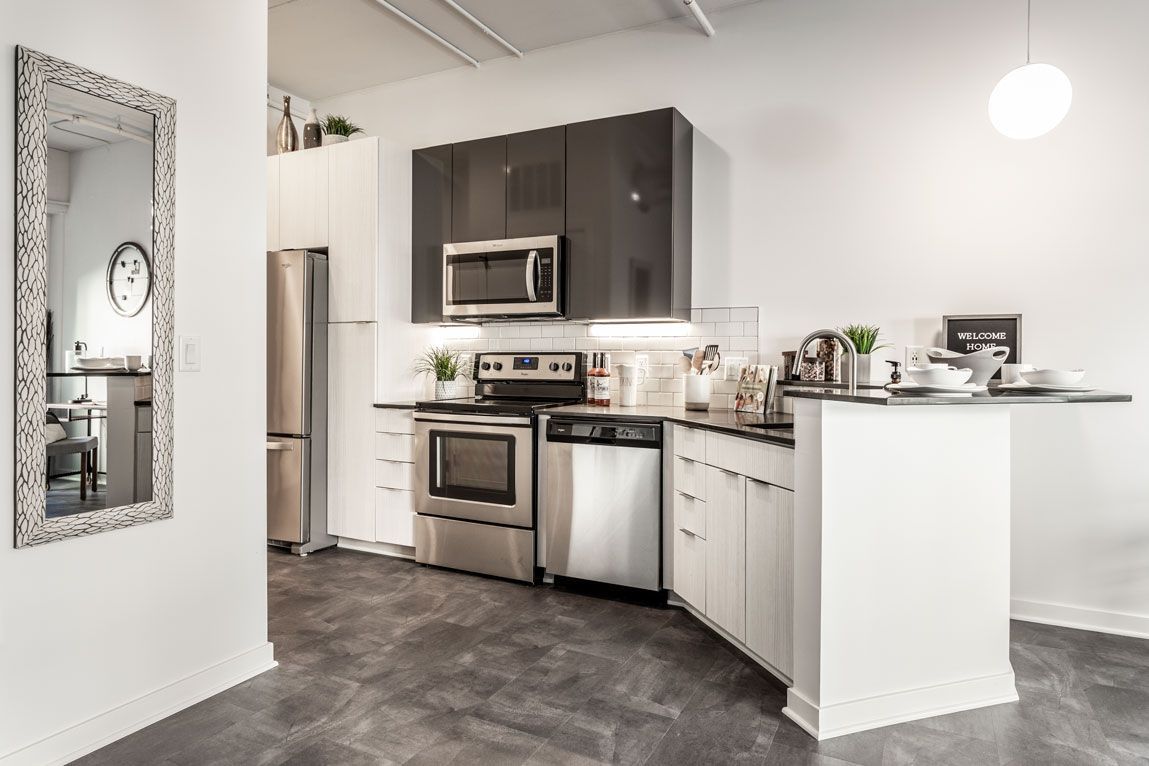 Here at Vim + Vigor Lofts in Wisconsin. A modern kitchen features two-tone cabinetry, stainless steel appliances, bright lighting, sleek counters, and stylish loft-inspired details.