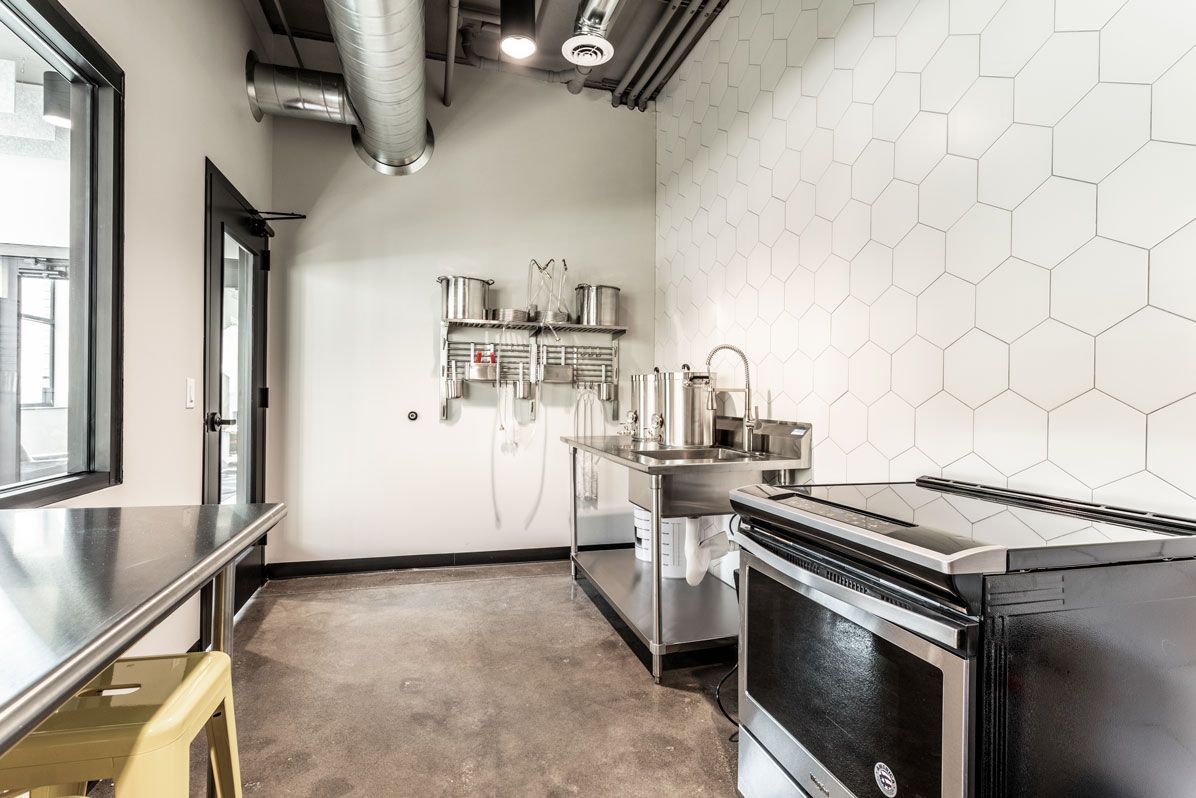 Here at Vim + Vigor Lofts in Wisconsin. A modern prep space features stainless steel surfaces, hexagon tile, industrial details, and a clean, functional community layout.