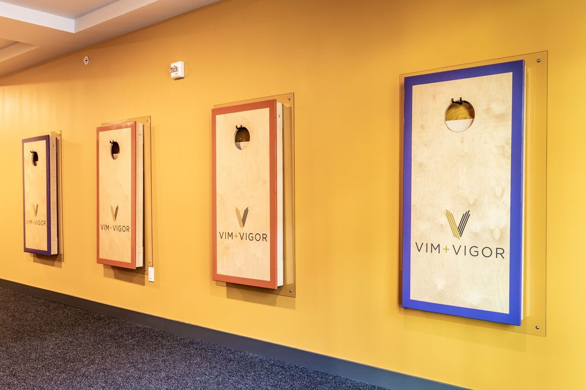 Here at Vim + Vigor Lofts in Wisconsin. A bright game area features yellow walls, branded boards, soft carpeting, and a fun, welcoming community atmosphere.