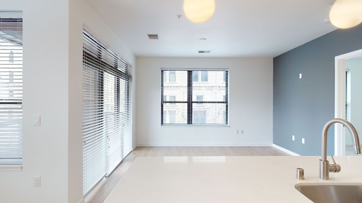 Here at Vim + Vigor Lofts in Wisconsin. A bright open living area features large windows, warm wood-style flooring, a modern gray accent wall, and a spacious kitchen island.