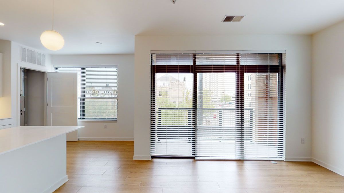 Here at Vim + Vigor Lofts in Wisconsin. A bright open living space features warm wood-style flooring, large balcony doors, modern blinds, and a spacious kitchen island.
