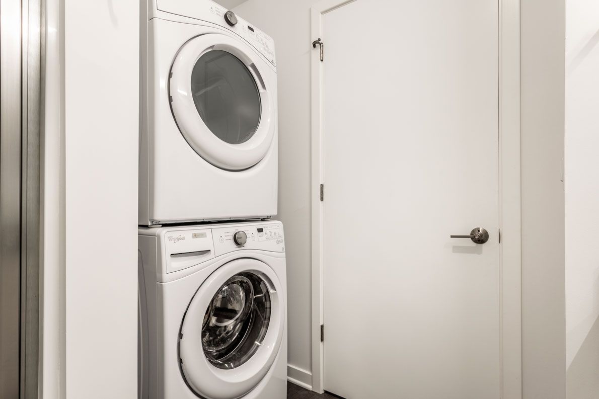 Here at Vim + Vigor Lofts in Wisconsin. A convenient in-home laundry area features a stacked washer and dryer, bright white walls, and a clean modern layout.