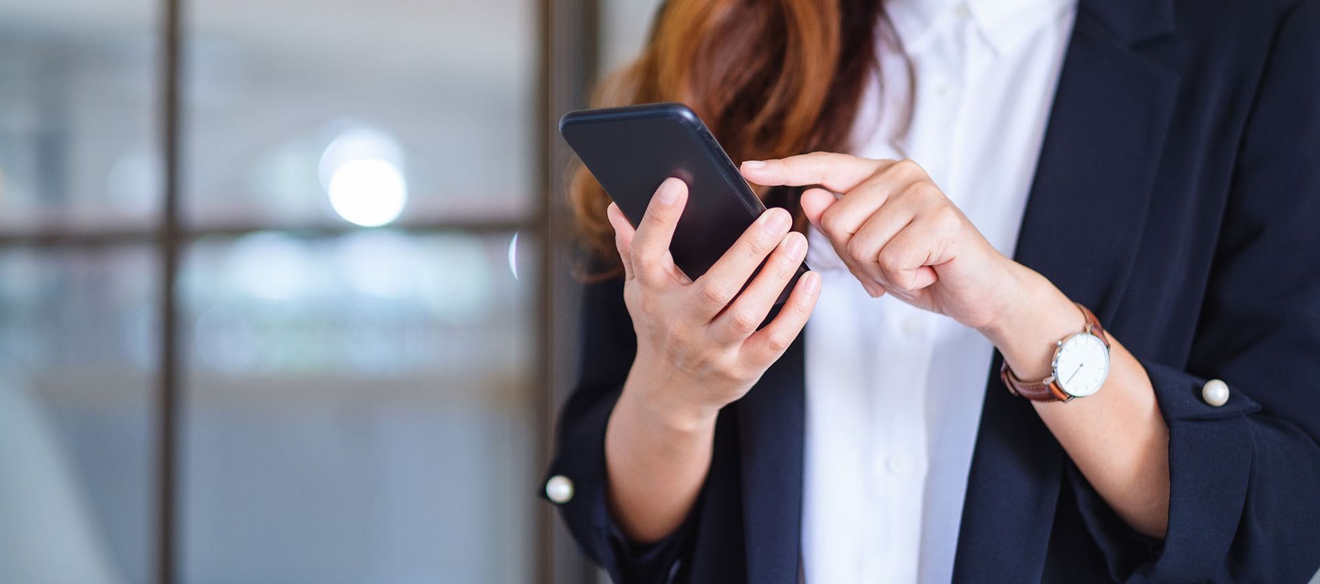 Woman in a blazer using a smartphone indoors. She is tapping the screen with her finger.