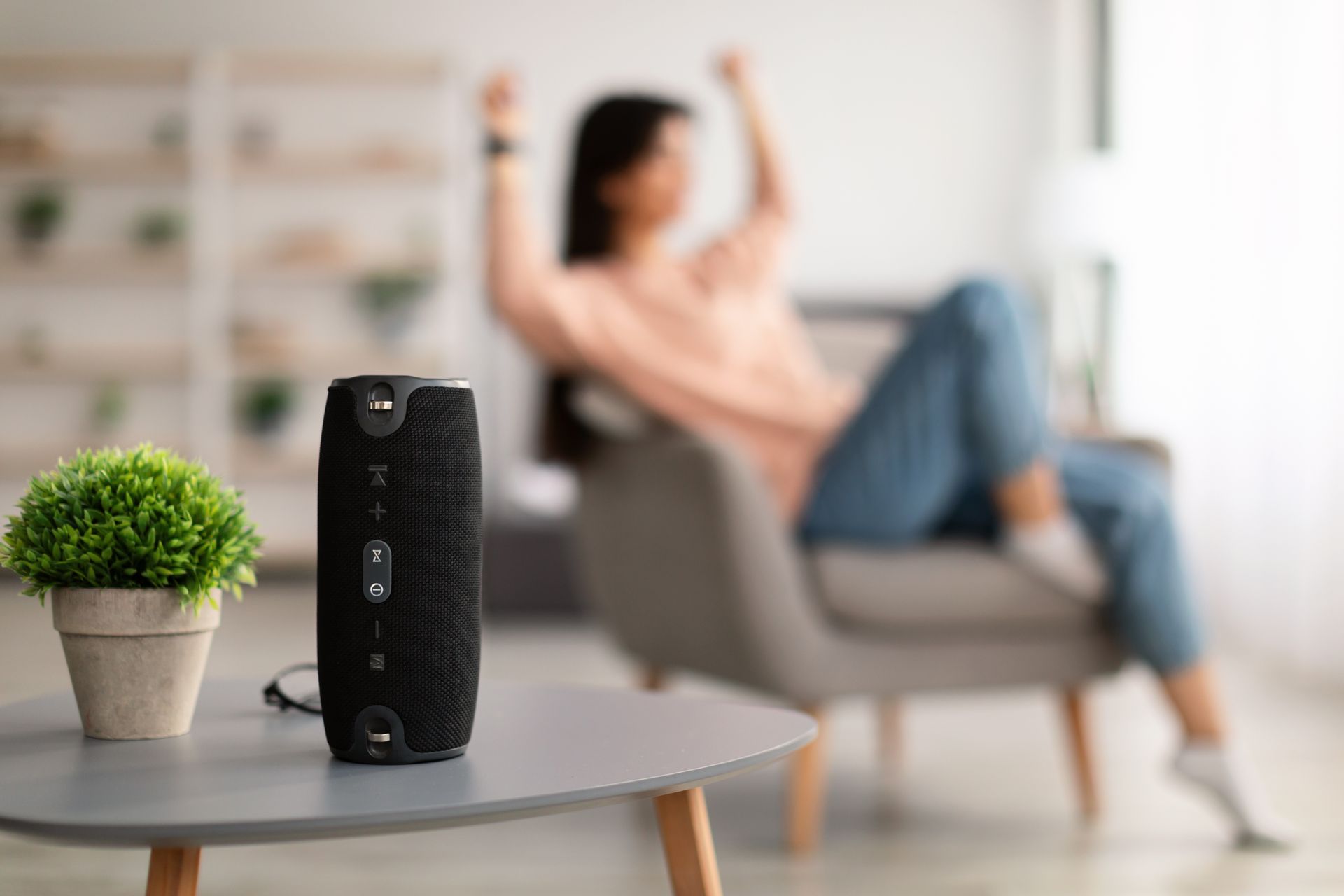 Two black speakers, books, remote, and tablet on a wooden surface against a gray wall.