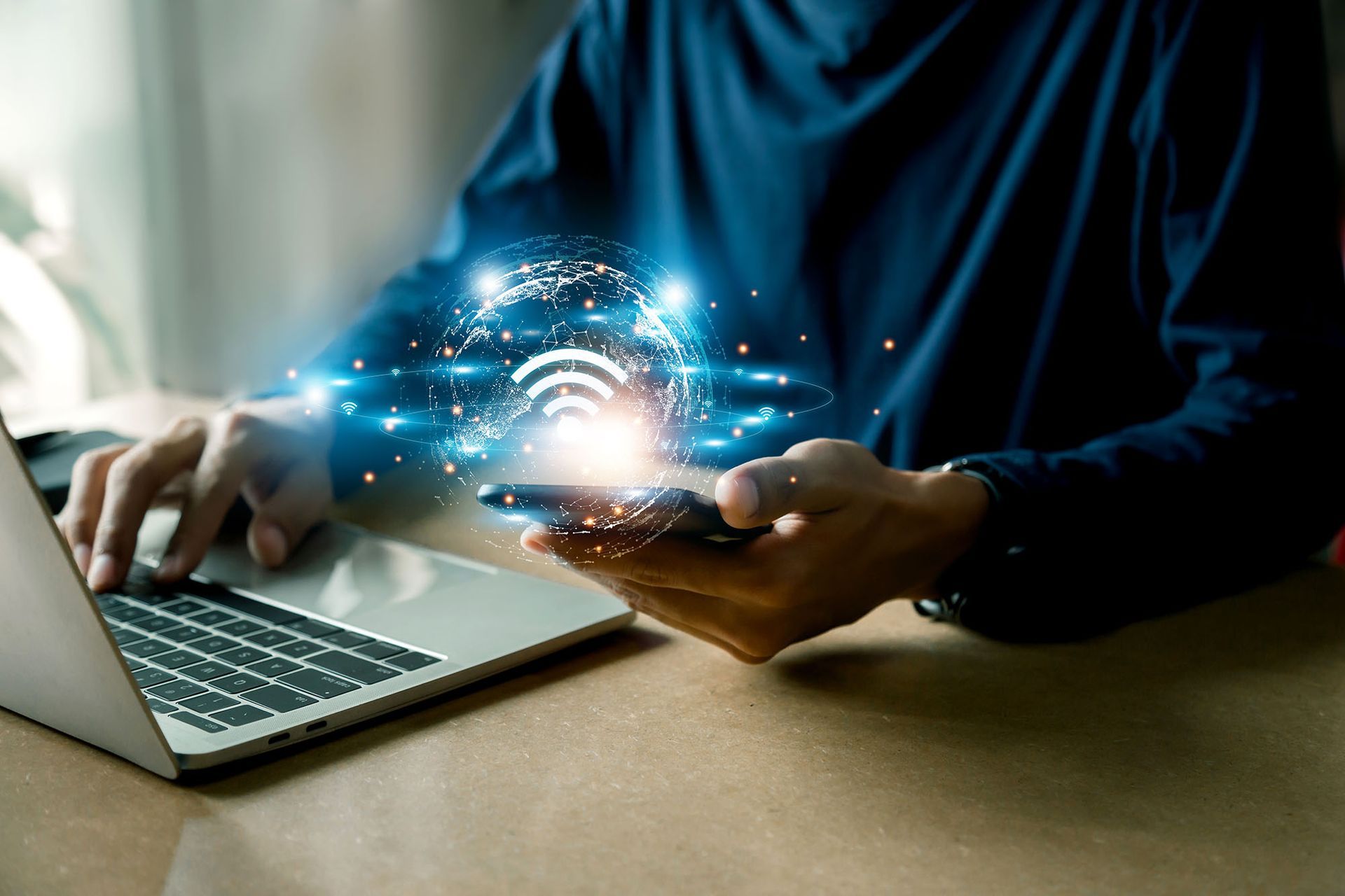 Person using laptop and smartphone with glowing WiFi signal emanating from the phone.